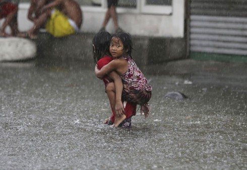 Các em bé cõng nhau dọc theo con đường ngập nước do mưa bão ở Mandaluyong, phía đông Manila, Philippines (Ảnh AP).